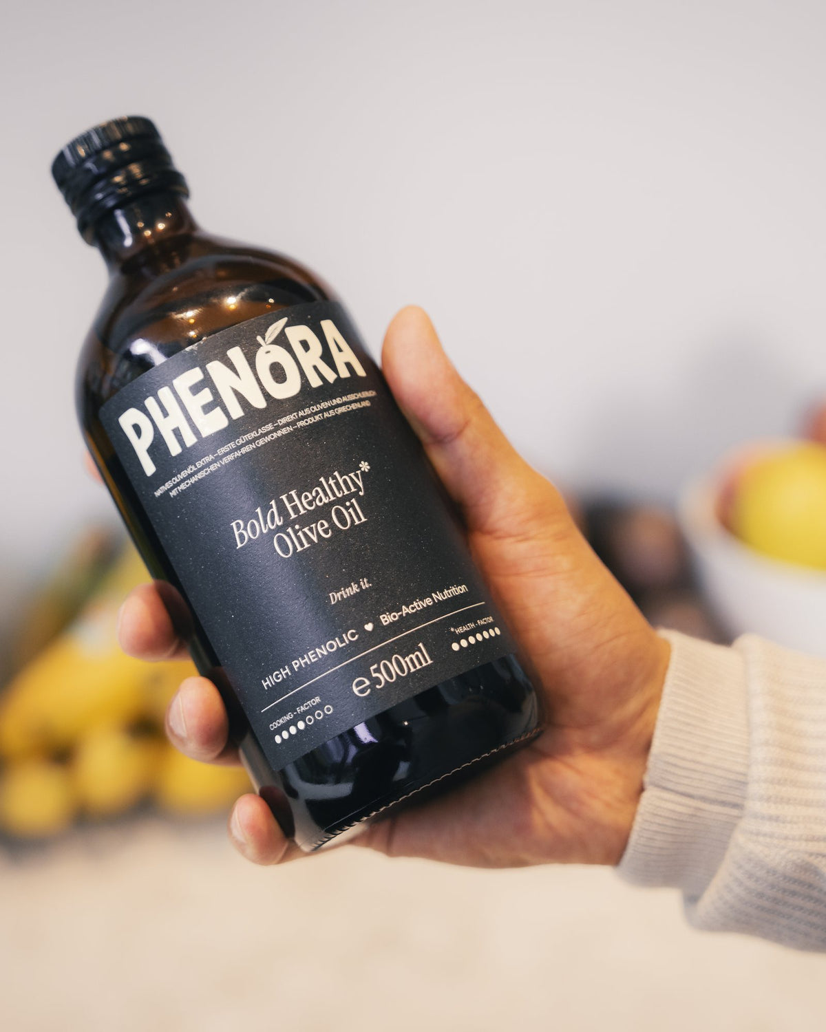 Hand hält eine Flasche Phenora Bold in einer hellen Küche